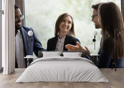 Laughing employees warmly welcoming young lady intern on workplace, friendly teammates congratulating woman coworker with promotion, partners praising businesswoman for creating successful project Wall mural