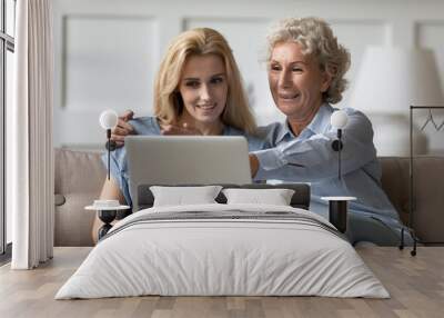 Look, mommy, it is easy. Caring grown up daughter teaching explaining retired mother how to work with laptop apps, happy old grandmother sits on couch with adult grandchild watching video on pc screen Wall mural