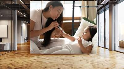 Loving Asian young mother and little girl playing doctor in bedroom together, caring mum using syringe, making prick, injection to adorable toddler child daughter, family enjoying leisure time Wall mural