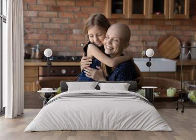 Loving cute little girl child hug sick cancer patient bald mother cooking healthy food salad in kitchen together, caring small daughter embrace show love support to ill mom, feel grateful thankful Wall mural