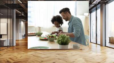 Loving young Caucasian father and little biracial daughter cook together at home, caring dad and small African American girl child prepare healthy food salad for breakfast in modern renovated kitchen Wall mural