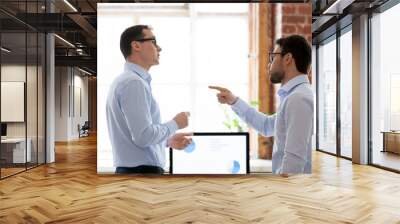 Mad male colleagues have disagreement in office arguing on work issues, furious millennial employee point at coworker blaming for mistake or failure, businessman accuse partner disputing at workplace Wall mural