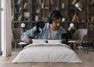 Man in headphones playing acoustic guitar, recording video on smartphone standing on tripod, using professional microphone, blogger or music teacher shooting course in home studio, sitting at desk Wall mural