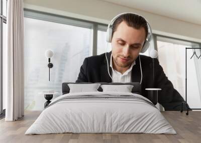 Man in headphones writing with pen at work desk. Entrepreneur takes part in online meeting or conference, live stream, learning foreign languages. Businessman listens music while working in office Wall mural