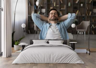 Meeting friday. Happy young guy freelancer enjoy calm moment when task is done relax rest stretch back hold hands over head. Serene millennial man recline on chair with closed eyes take break in work Wall mural