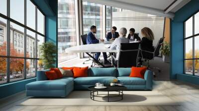 Millennial diverse different aged business team meeting in modern office space. Partners, stakeholders, colleagues negotiating at conference table at panoramic glass wall window Wall mural