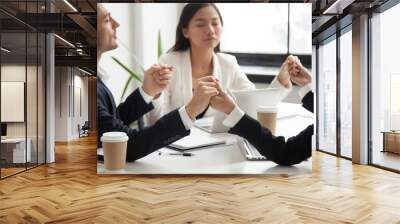 Mixed business team holding hands, meditating, praying for success, managing work stress. Colleagues relaxing, reaching balance, wellness. Renewing energy, improving mental state, teambuilding concept Wall mural