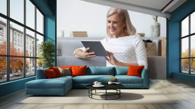 Modern elderly woman using tablet relaxing at home Wall mural