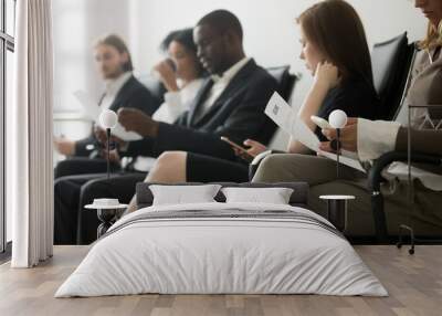 Multi-ethnic applicants sitting in queue preparing for interview, black and white vacancy candidates waiting on chairs holding resume using smartphones, human resources, hiring and job search concept Wall mural