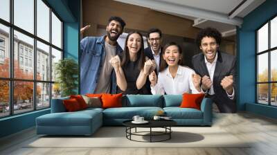 Multiethnic business team of excited project colleagues celebrating teamwork success, successful startup, making winning fist hand gestures, laughing, shouting for joy at camera Wall mural