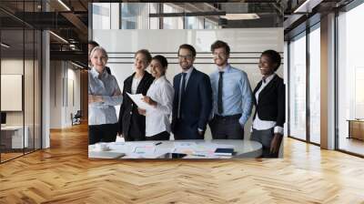 Multiethnic employees standing in modern office boardroom looking at camera making team picture, smile pose for photo at workplace, show unity and cooperation. Teamwork, leadership and career concept Wall mural