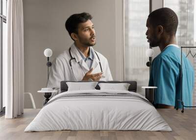 Multiethnic practitioner and surgeon men discussing diagnosis, medical examination result, using tablet computer, talking in clinic, hospital office. Indian doctor instructing nurse Wall mural