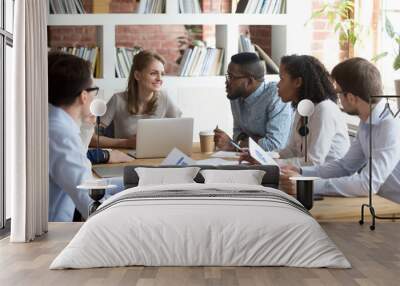 Multiracial millennial colleagues brainstorm discussing startup ideas during briefing in boardroom, female CEO hold business meeting with diverse employees, negotiating analyzing report or stats Wall mural