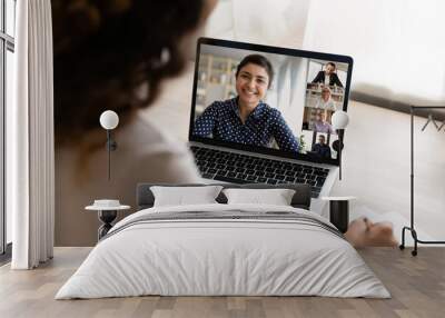 Over shoulder view of woman look at laptop screen have webcam team meeting or briefing with colleagues. Female employee talk on video call on computer, engaged in digital virtual event with coworkers. Wall mural