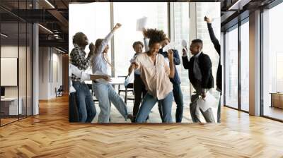 Overjoyed African American business people celebrating success, throwing papers, happy diverse employees excited by business achievement, good news, dancing in modern office, rejoicing victory Wall mural