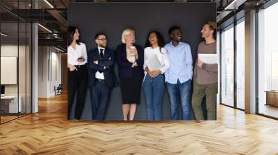 Overjoyed diverse multiethnic businesspeople stand posing near black wall have fun together joking at break, excited happy multiracial colleagues laugh and joke, unity, team spirit concept Wall mural