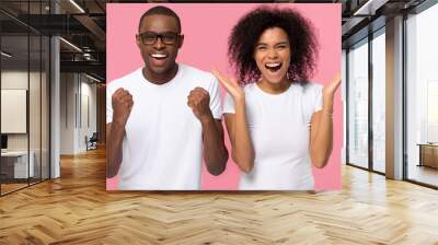 Overjoyed excited african american family couple winners celebrate win enjoy victory rejoice success, happy ecstatic euphoric black man and woman screaming with joy isolated on pink studio background Wall mural