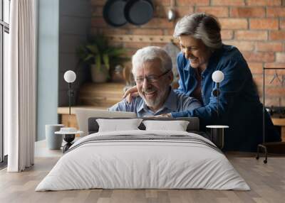 Overjoyed mature couple using laptop together, reading good news in email or message, shopping sales, smiling senior woman and man wearing glasses looking at screen, having fun with computer Wall mural