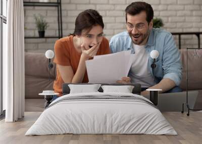 Overjoyed young couple reading letter together, happy surprised man and woman excited by received amazing good news, approved mortgage loan, money refund, great investment or insurance offer Wall mural