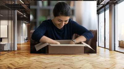 Overjoyed young Indian woman open unpack cardboard box with internet order shopping online from home. Excited millennial ethnic female buyer unbox package buying on web. Delivery service concept. Wall mural