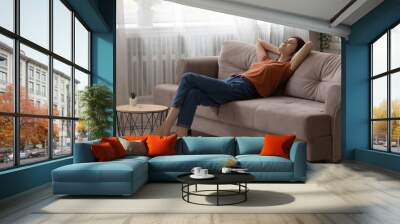 Peaceful young woman relaxing on comfortable couch at home, calm tranquil attractive female taking nap, resting with closed eyes on cozy sofa in modern living room, leaning back, daydreaming Wall mural