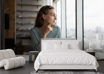 Pensive young female employee work on computer in office look in distance thinking pondering of career opportunities. Thoughtful woman worker distracted from laptop job making plans or decision. Wall mural