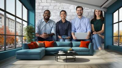 People and gadgets diversity. Group portrait of confident happy young friends men and women of caucasian indian african ethnicities sitting in row looking at camera holding phones computers in hands Wall mural