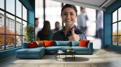 Photo portrait of happy Indian female business leader gesturing like, showing thumb up. Team working in background. Satisfied client woman gives approval positive feedback, recommends company service Wall mural