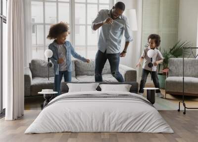 Playful young african American dad dancing playing in living room with two little children, happy biracial father have fun dancing with small kids son and daughter, enjoy weekend at home together Wall mural