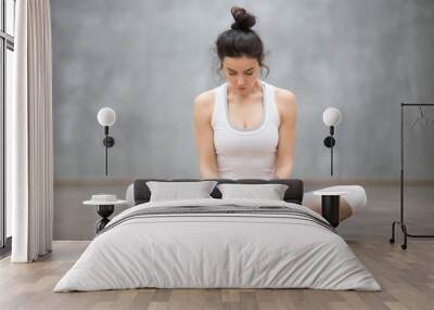 Portrait of beautiful young woman with floral tattoos working out against grey wall, doing yoga or pilates exercise, sitting in baddha konasana, bound angle, cobbler, butterfly pose. Full length shot Wall mural