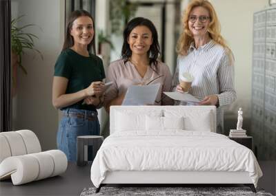 Portrait of diverse multiracial coworkers stand holding paperwork brainstorming in modern office, group picture of multiethnic businesspeople female employees pose together cooperating at workplace Wall mural