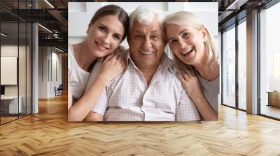 Portrait of happy adult family sit rest on couch smile for picture at home together, overjoyed senior parents hug embrace grownup daughter relax enjoy leisure weekend, look at camera posing Wall mural