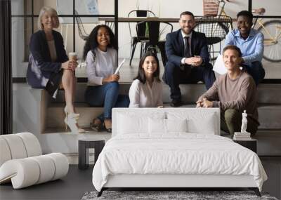 Portrait of happy mature and young coworkers sitting on stairs. Wall mural