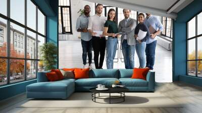 Portrait of happy millennial diverse professional team in loft office space. Group of multi ethnic employees gathering for corporate meeting and teamwork, looking at camera, smiling. Full length Wall mural