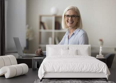 Portrait of happy successful mature businesswoman posing for camera seated at workplace desk with laptop. Teleworking or freelance, workflow using modern technology, e-mailing, remote communication Wall mural