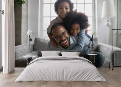 Portrait of overjoyed young playful african American father have fun in living room with two small ethnic children, excited biracial dad play with little kids, engaged in funny activity together Wall mural