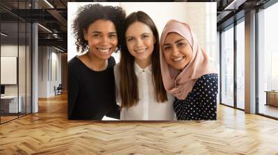 Portrait of smiling multiethnic female employees colleagues hug embrace pose together in international office, happy diverse multiracial women interns students show unity and friendship in relations Wall mural