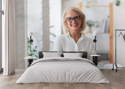 Portrait of smiling senior businesswoman in glasses standing posing in modern office, happy confident middle-aged female employee or CEO look at camera show confidence and success at workplace Wall mural