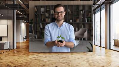 Portrait of smiling young businessman hold soil and small plant launch startup project or activity. Happy millennial male employee or CEO with seedling sprout in hands. Growth, development concept. Wall mural