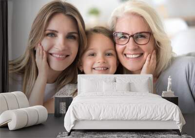 Portrait of three generations of women look at camera posing for family picture, cute little girl hug mom and granny enjoy time at home, smiling mother, daughter and grandmother spend weekend together Wall mural