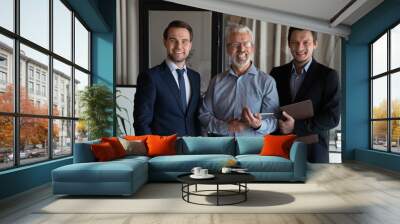 Portrait of three smiling confident businessmen employees startup team with mature executive standing in office, businesspeople workers coworkers group looking at camera, posing for corporate photo Wall mural