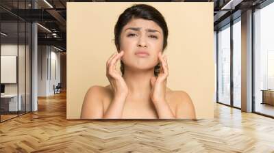 Portrait of unhappy young Indian woman isolated on yellow studio background touch face worry about pimples wrinkles. Upset mixed race female think of botox treatment. Facial skincare concept. Wall mural