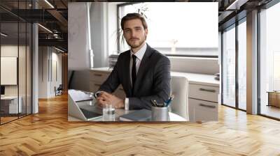 Portrait of young confident skilled handsome male manager in formal suit sitting at workplace with computer, motivated millennial businessman leader employee worker looking at camera in office. Wall mural