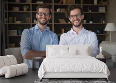 Positive confident family business partner men portrait. Happy handsome young adult twin brothers in glasses and office shirts posing together at home with arms crossed, looking at camera, smiling Wall mural