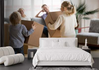 Rear view at kids playing with boxes on moving day, small brother and sister running holding belongings packing unpacking in new home, happy playful children having fun together enjoying relocation Wall mural