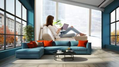 relaxed woman using laptop in luxury home living room with big window, enjoying working, internet sh Wall mural