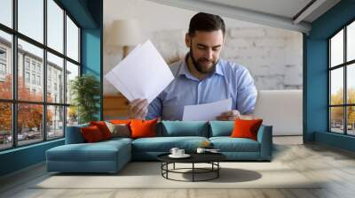 Satisfied smiling business man doing paperwork at home workplace. Entrepreneur reading financial reports, reading documents. Tenant making payment for rent, reviewing bills, bank mortgage notice Wall mural