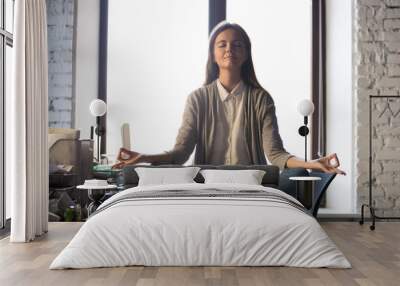 Serene calm business woman sit on office desk taking break for meditation, mindful employee doing yoga exercise in lotus pose for relaxation at workplace, no stress relief, balance at work concept Wall mural