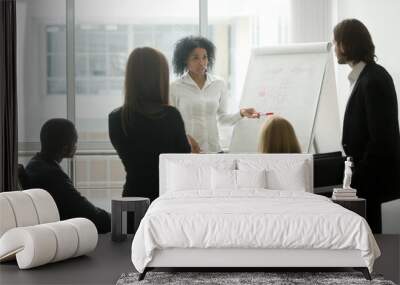 Serious african female leader or coach gives presentation of new marketing plan at sales team meeting, black employee explains colleagues new client management strategy idea at group office training Wall mural