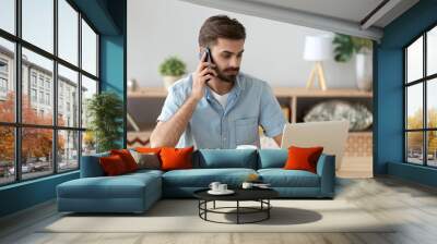 Serious businessman sitting at the desk typing chatting using computer and talking by cellphone. Confident employee hard working busy during work day solving business matters agent talking with client Wall mural